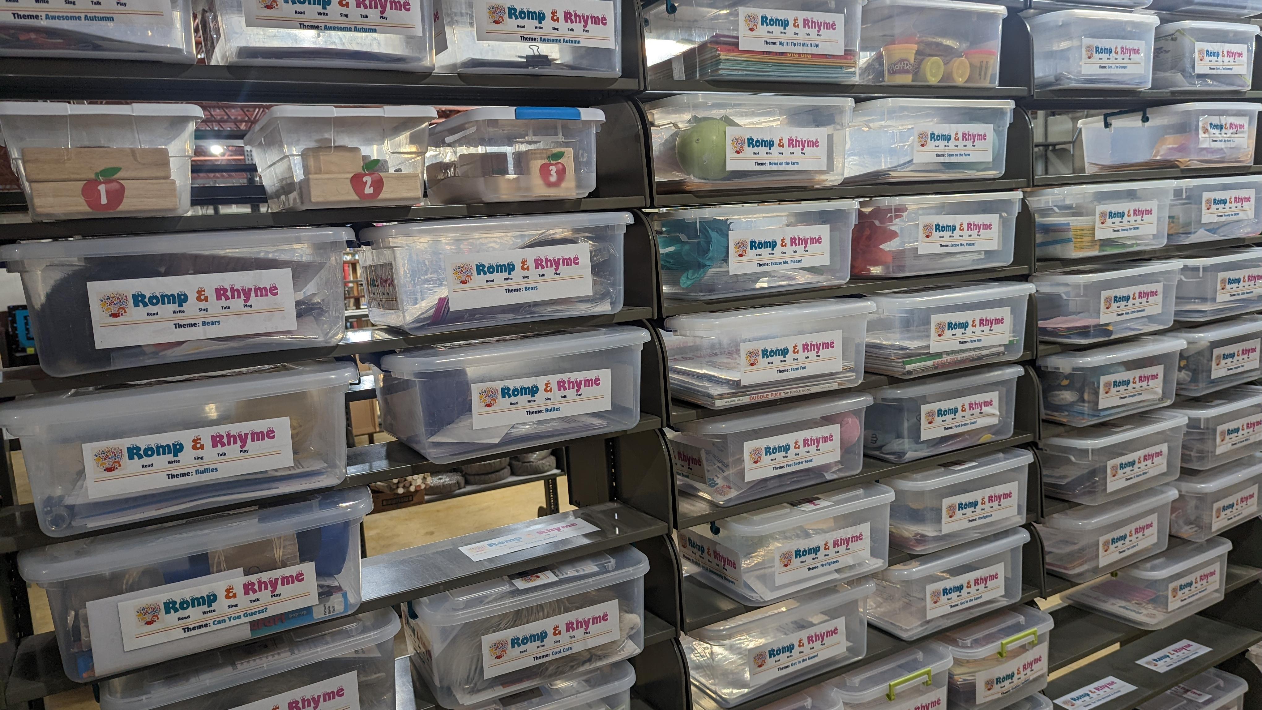 A photograph of dozens of transparent plastic bins, labeled "Romp and Rhyme" on each end.