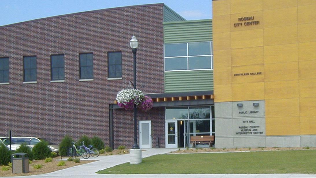 Exterior of municipal building, red brick on the left side, yellow tile on the right, with green siding around the central door.