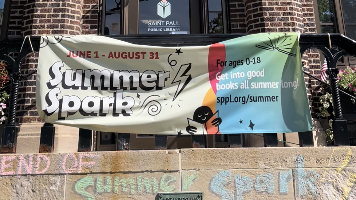 A photo of the St. Anthony Park Branch Library front entrance with their summer spark banner.