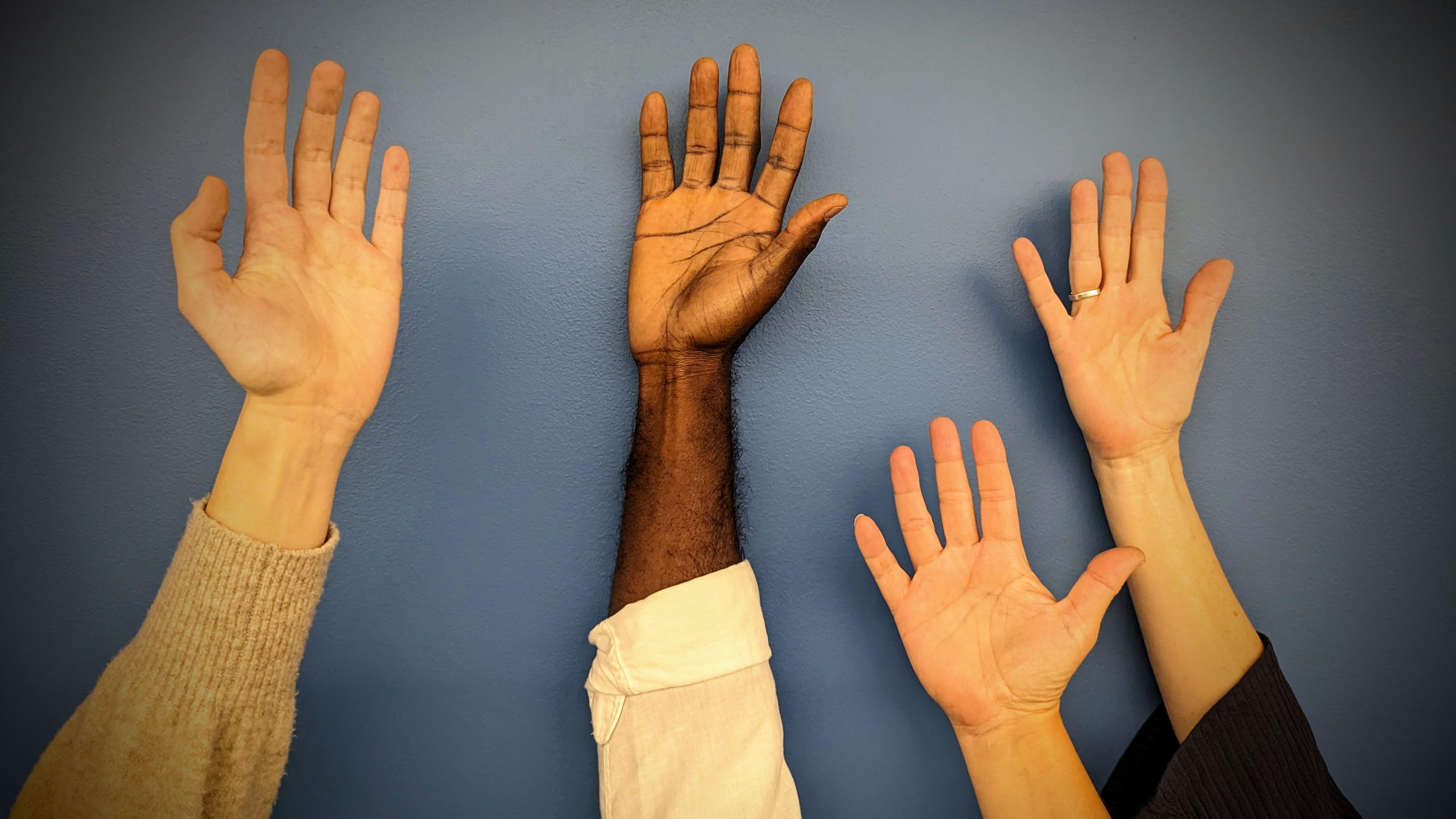 A photograph of four raised hands.