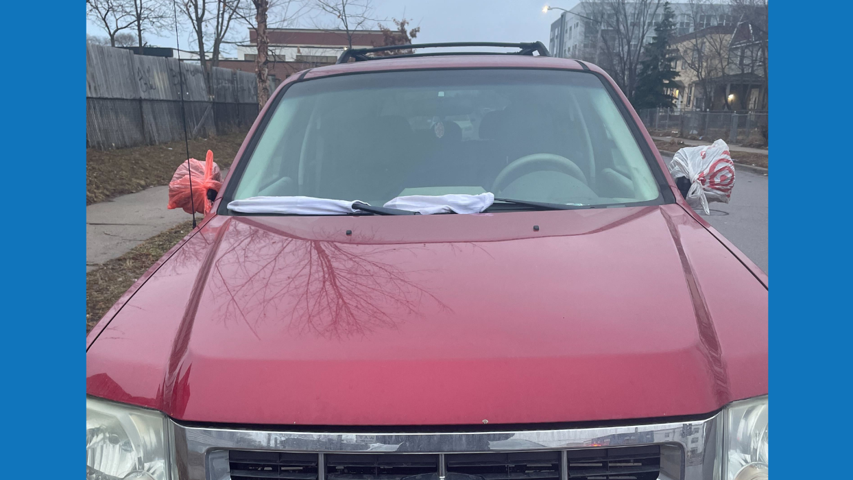 A photo of the front of red car with socks on windshield wipers and plastic bags on rearview mirrors.