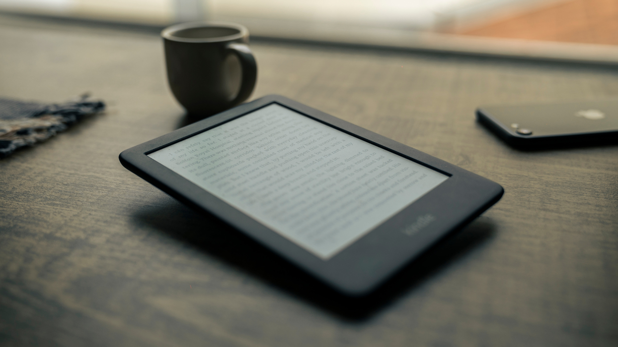 Image of ebook pulled up on a  kindle tablet next to a cup and an iPhone.