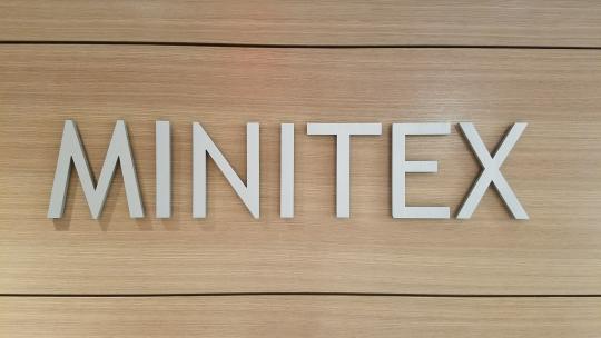 The "Minitex" sign in the entrance of Minitex's offices featuring silver all-caps lettering on a wood-panel background.