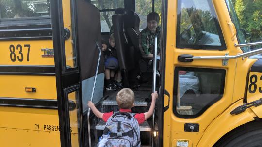 A photo of a kindergartner climbing aboard a yellow school bus.