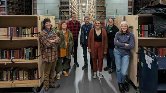 Eight library staff stand pose in front of the stacks in MLAC.