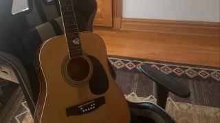 A photo of a wooden 12 string guitar and pick upon a gaming seat. 
