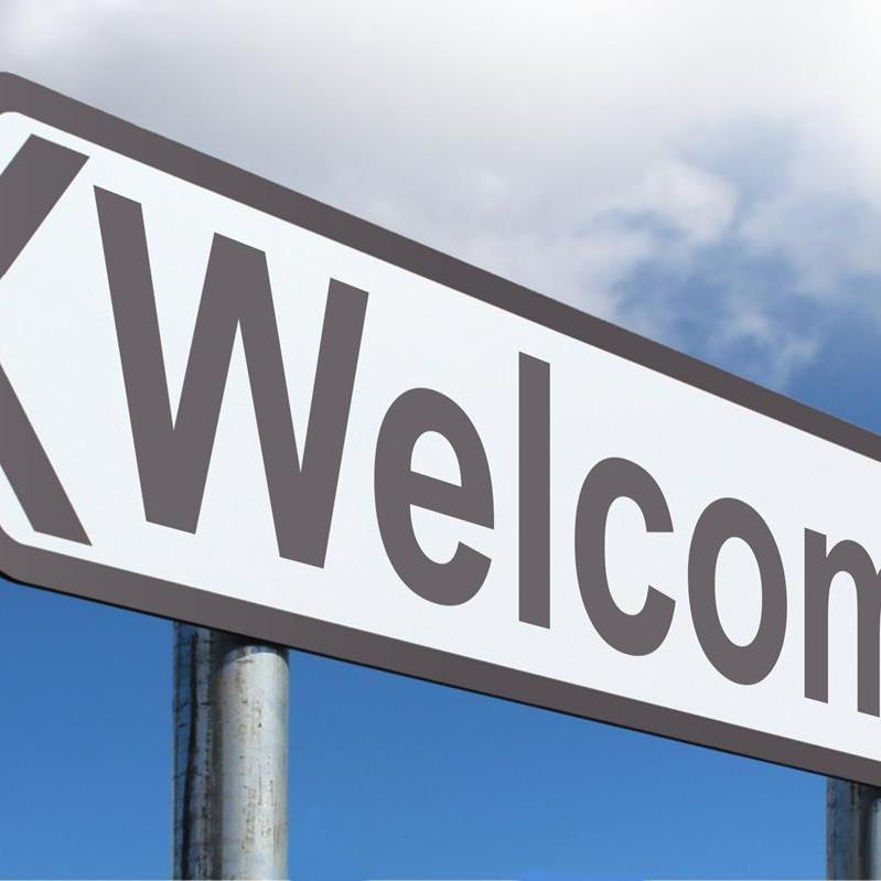 A photograph of a road sign with 'welcome' emblazoned in dark gray lettering.