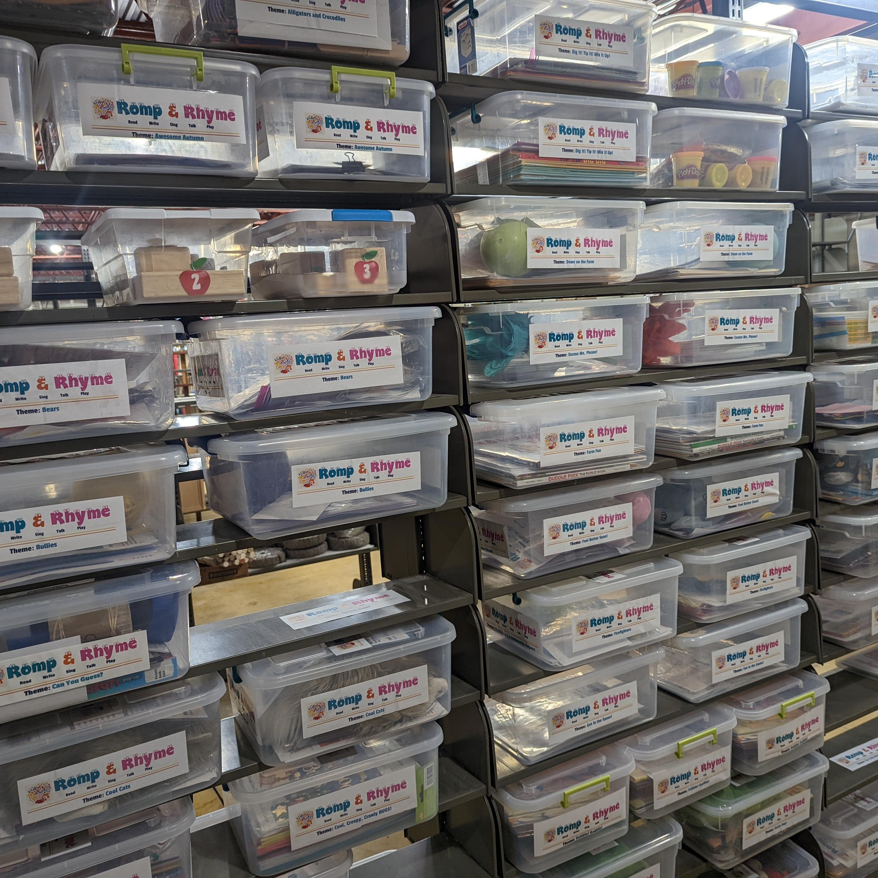 A photograph of dozens of transparent plastic bins, labeled "Romp and Rhyme" on each end.