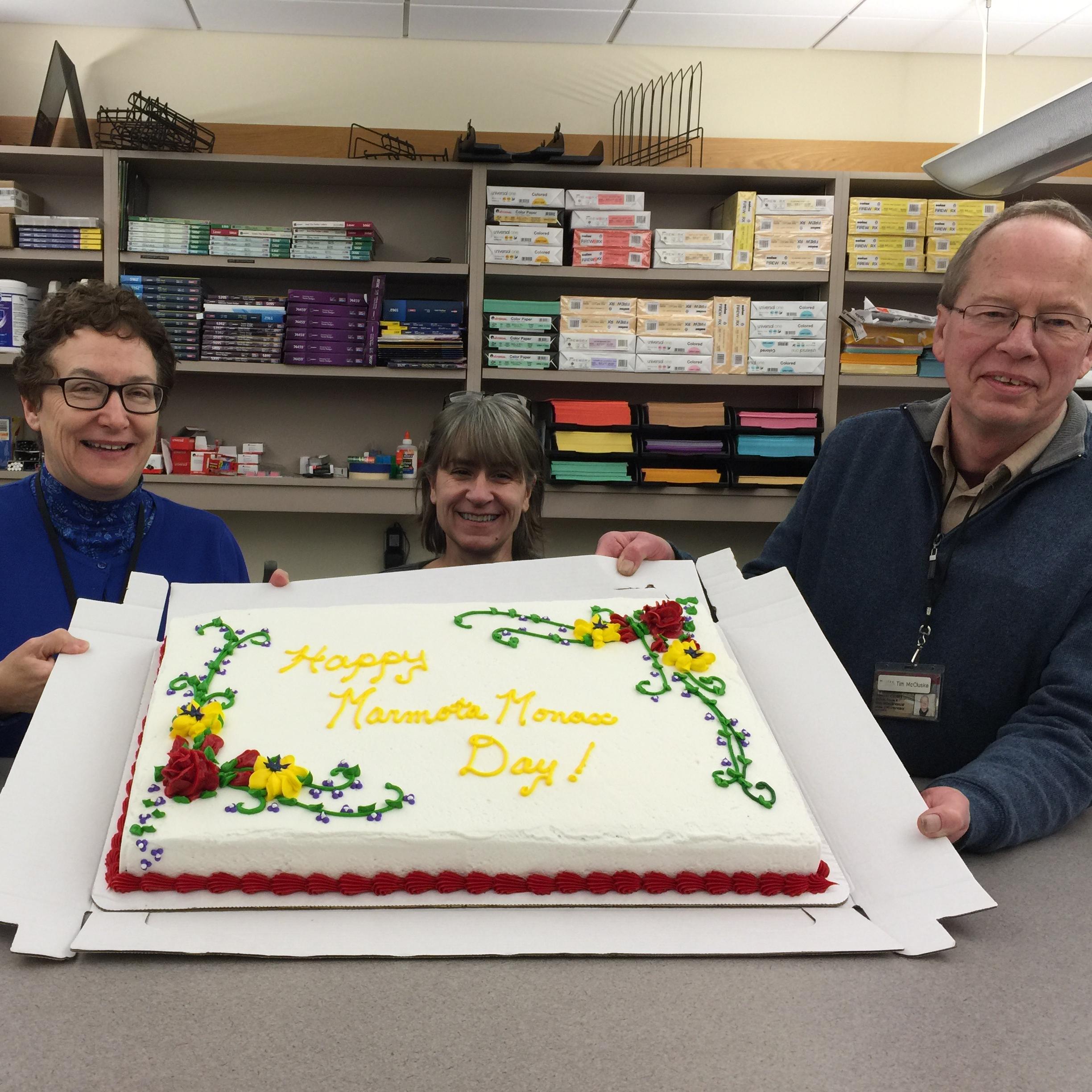 Three people display a cake commemorating Groundhog Day
