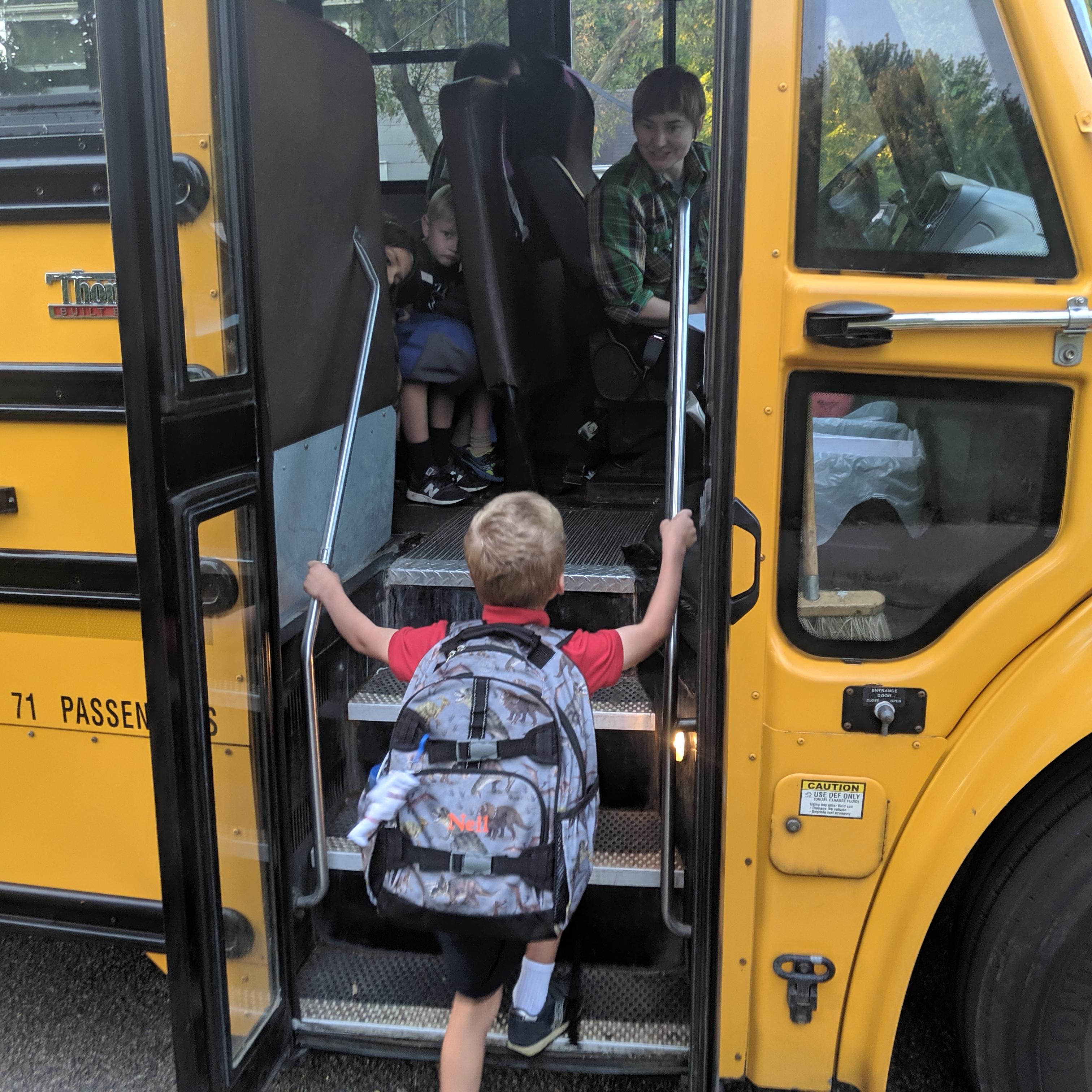 A photo of a kindergartner climbing aboard a yellow school bus.