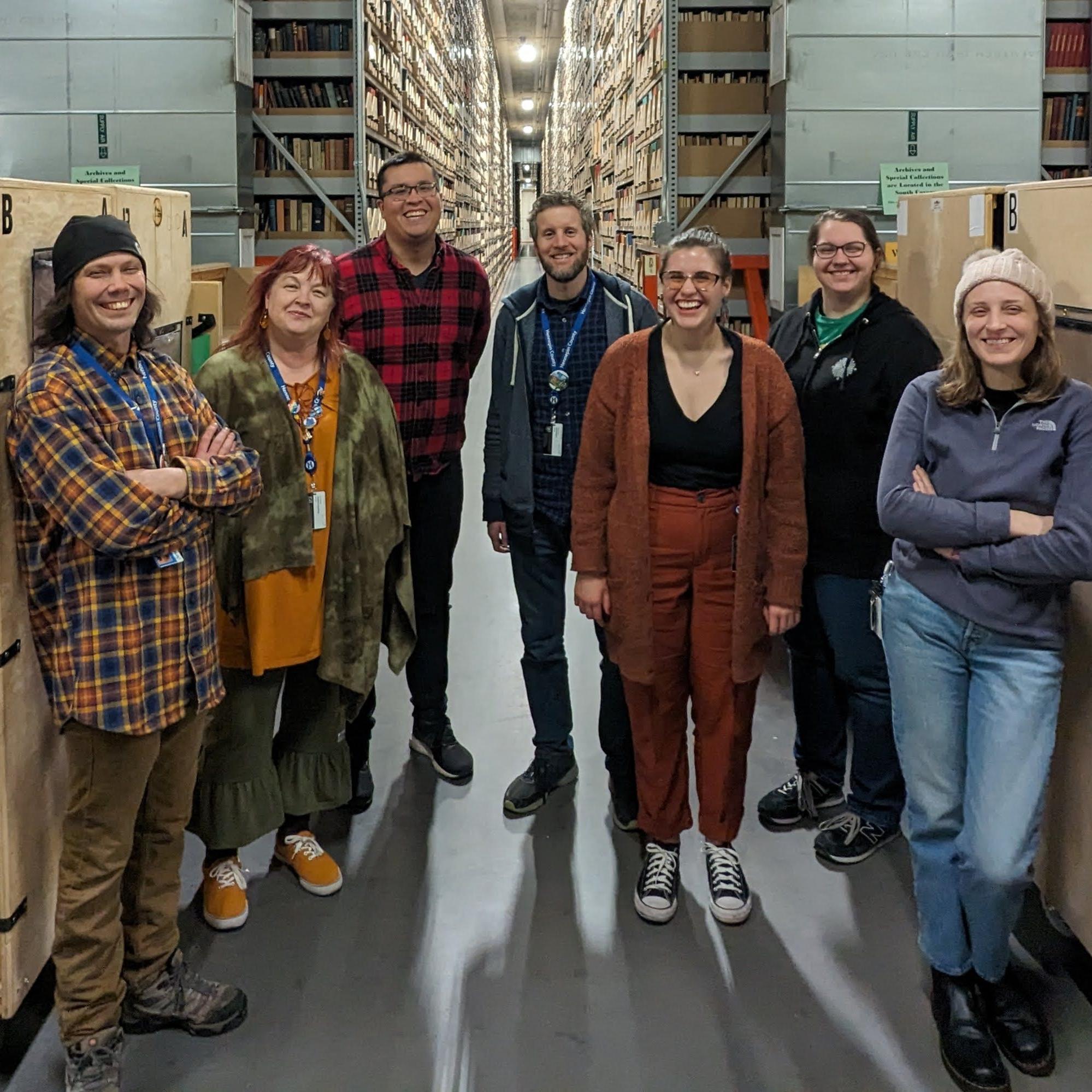 Eight library staff stand pose in front of the stacks in MLAC.