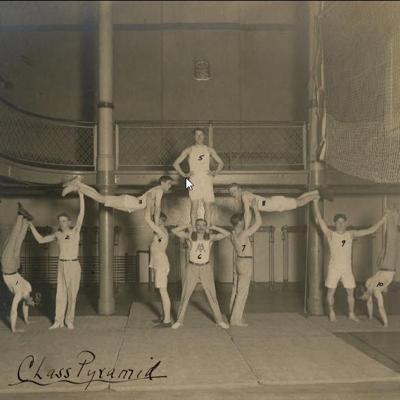 Eight men in exercise clothing balancing to form a gymnastic pyramid in a gymnasium